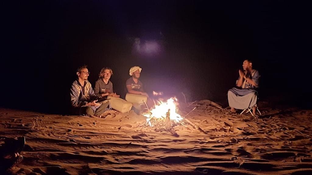Guests and guides around the campfire under a black desert sky, Sahara Morocco