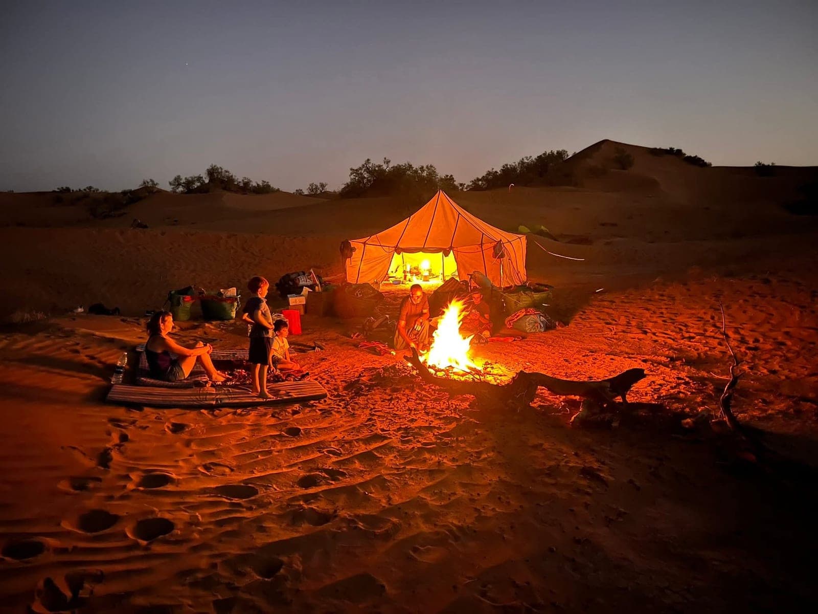 A family with young children around the campfire at our Sahara camp at dusk, guide tending the fire, Morocco