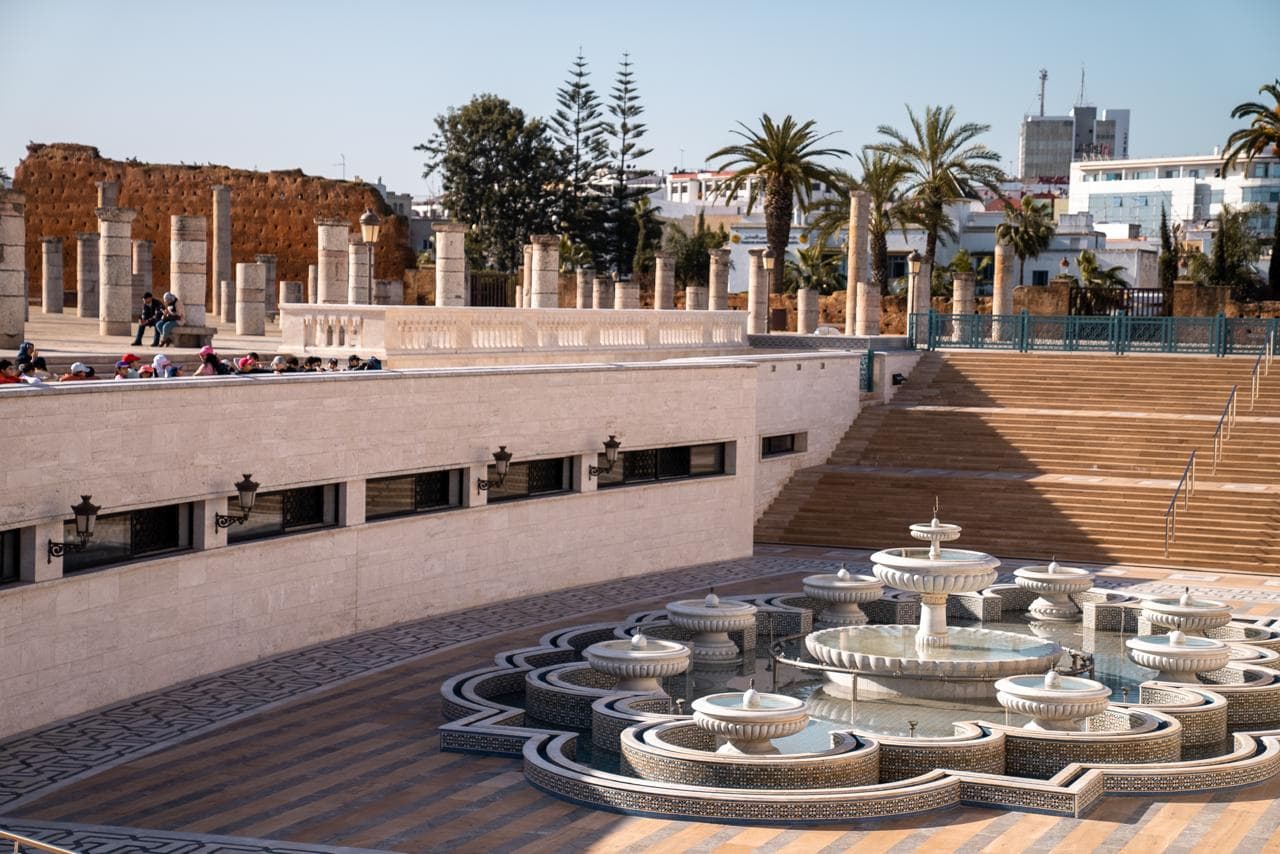 The tiled fountain court below the Hassan esplanade, school groups along the balustrade and the ruined mosque columns above, Rabat Morocco