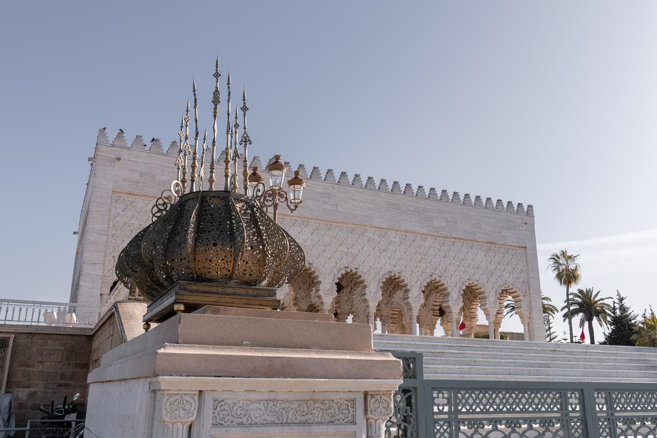 A pierced brass lantern on its plinth below the crenellated white marble wall of the Mausoleum of Mohammed V, Rabat Morocco