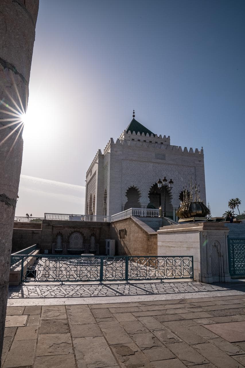 The green pyramid roof of the Mausoleum of Mohammed V with the sun flaring past a column of the Hassan mosque, Rabat Morocco