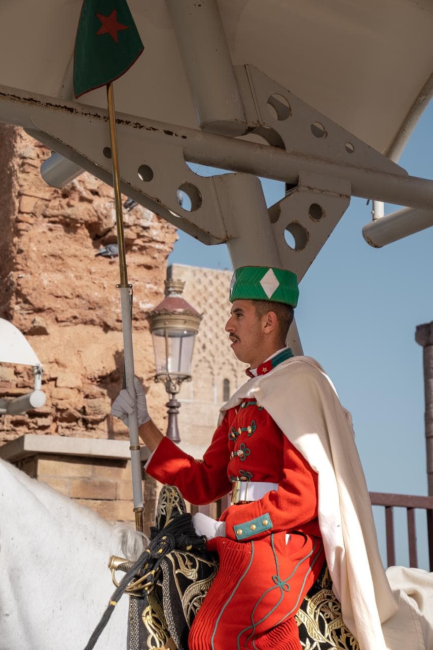 A Royal Guard cavalryman in red tunic and white cloak on a grey horse at the entrance to the Mausoleum of Mohammed V, Rabat Morocco