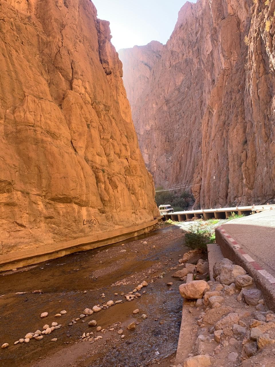 The Todra river running shallow over stones beside the gorge road under overhanging cliffs, Morocco