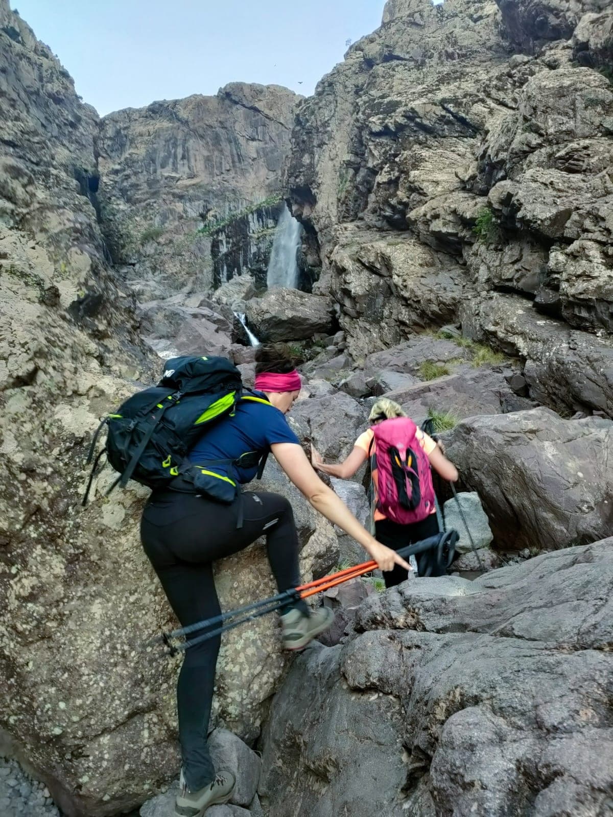 Trekkers scrambling a rocky gorge step with poles on a High Atlas route, Morocco