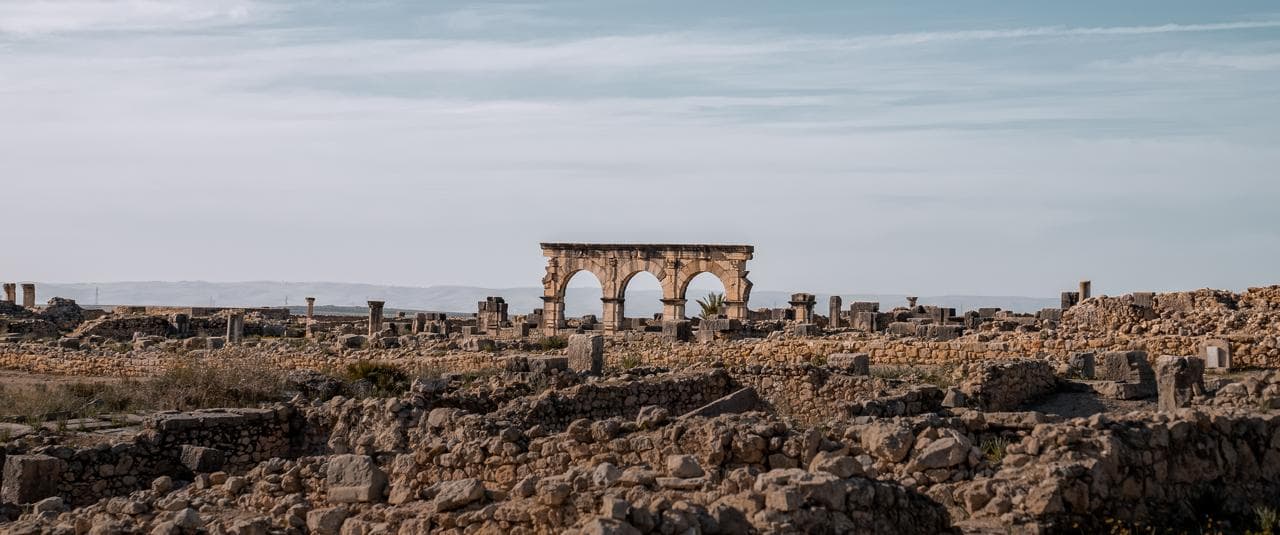 The Arch of Caracalla seen across the excavated street plan of Volubilis with the hills of the Rif behind, Morocco