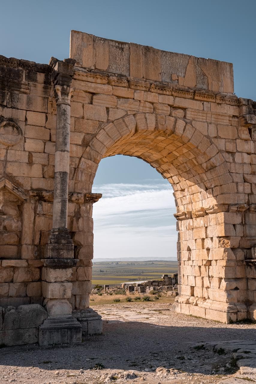 The Arch of Caracalla at Volubilis with its Latin dedication above and the Zerhoun plain framed through the opening, Morocco