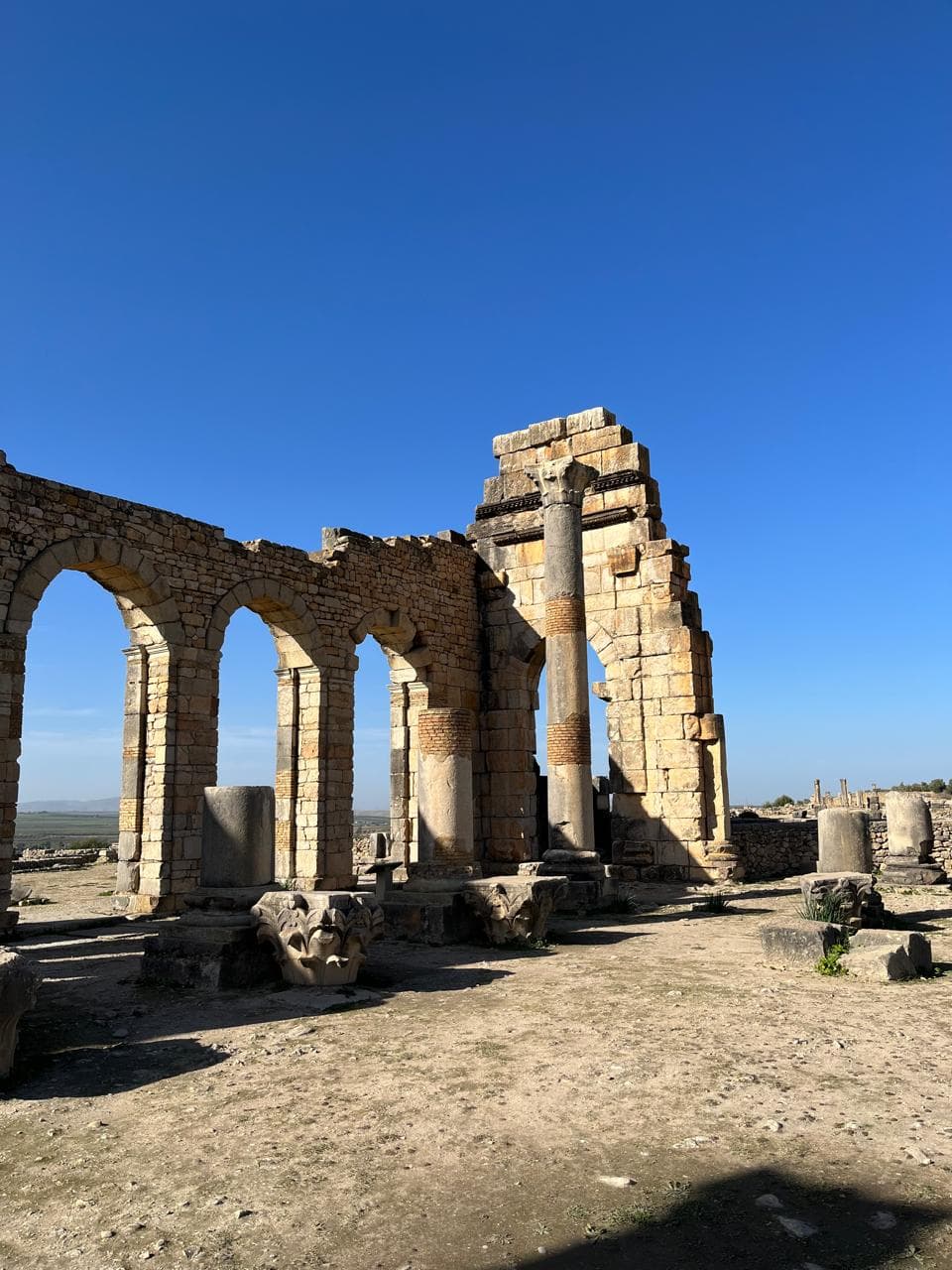The arched basilica of the Roman city of Volubilis with fallen Corinthian capitals in the foreground, Morocco
