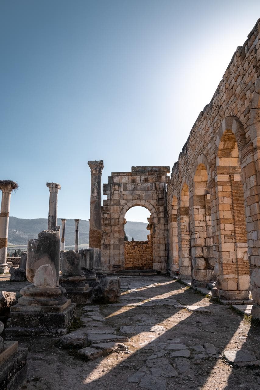 Morning shadows across the paved floor inside the basilica of Volubilis, the arched wall standing to full height, Morocco